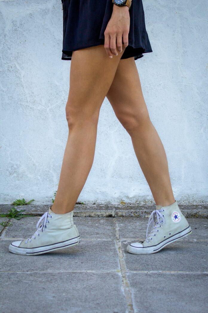 Photo by Apostolos Vamvouras a woman walking down a sidewalk wearing tennis shoes